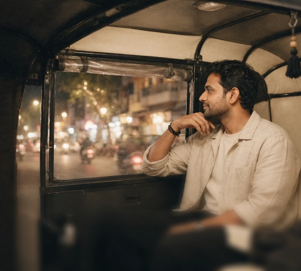 A man relaxes in the back of an auto-rickshaw at night with city lights outside.