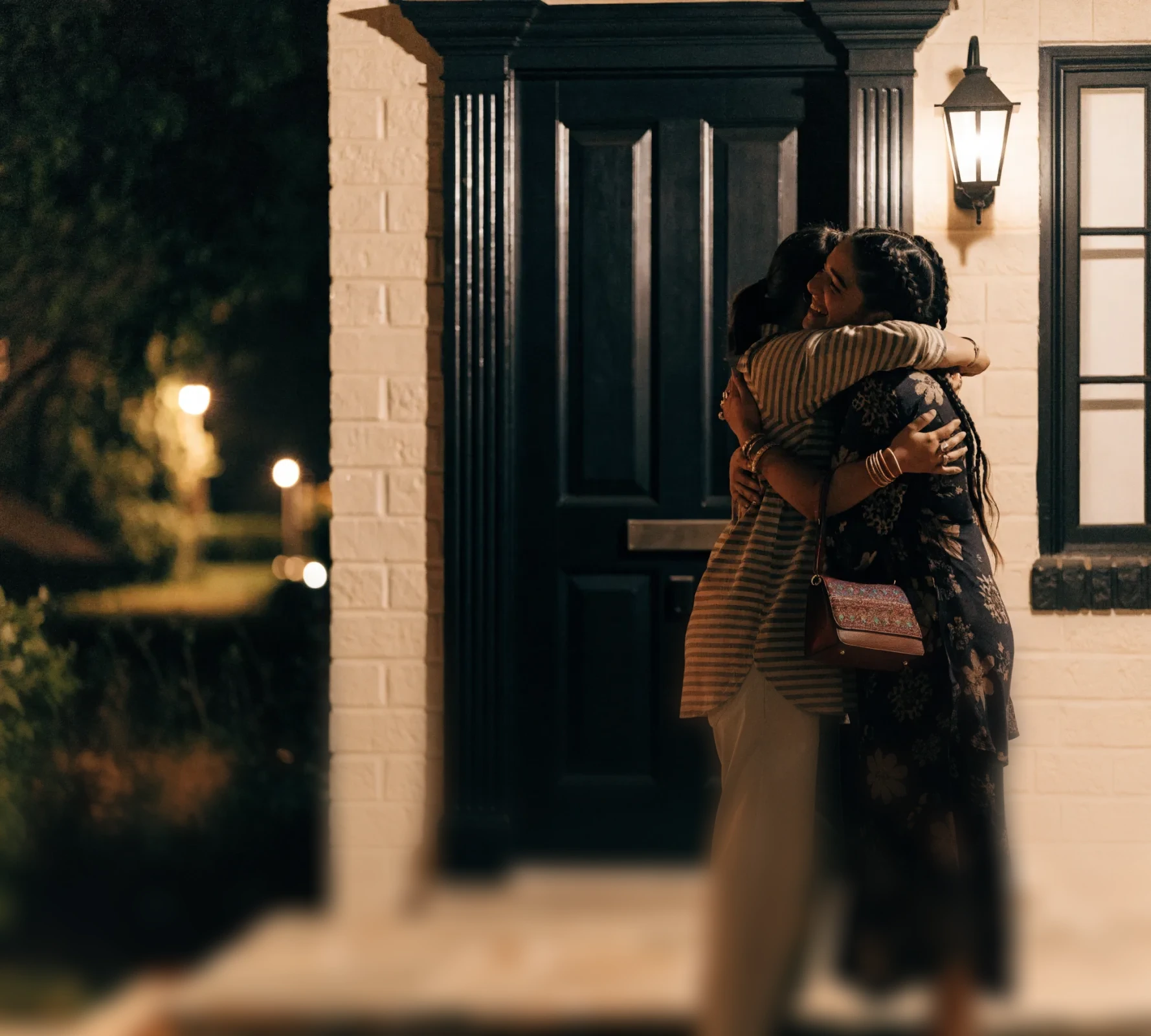Two friends hug at a front door at night, relieved to see each other.